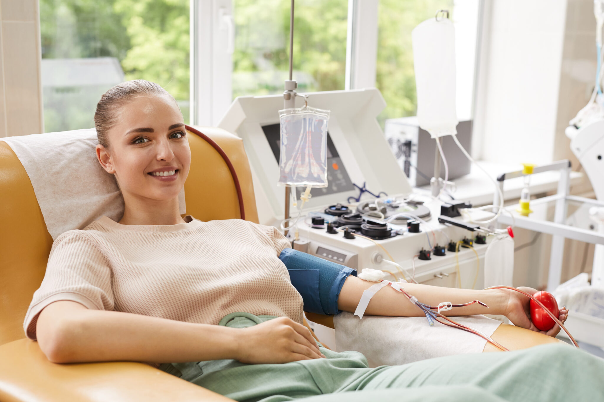 Portrait of young woman smiling at camera while lying on the couch and donating the blood at hospital